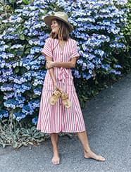 a woman in a pink dress standing in front of a lilac bush